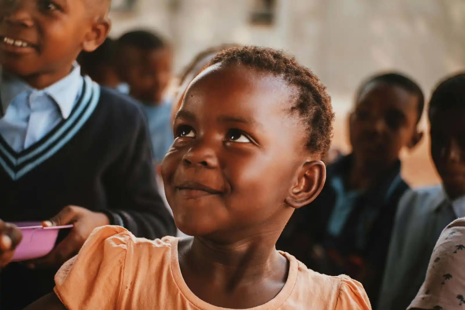 A young Nigerian schoolgirl smiling, classmates in uniform around her